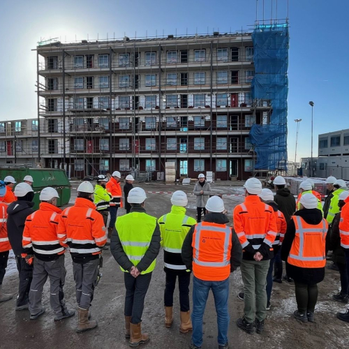 Groep bouwvakkers die luisteren naar hun leidinggevende met het bouwproject in de achtergrond