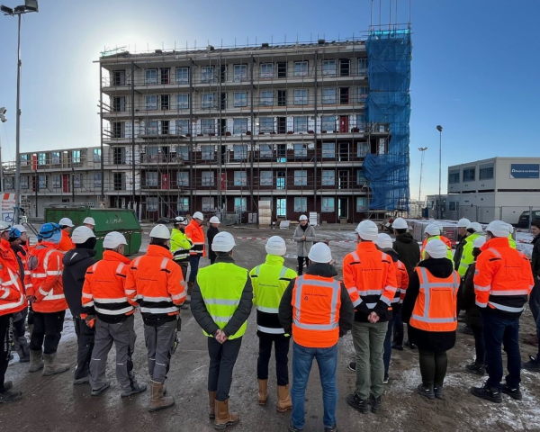 Groep bouwvakkers die luisteren naar hun leidinggevende met het bouwproject in de achtergrond